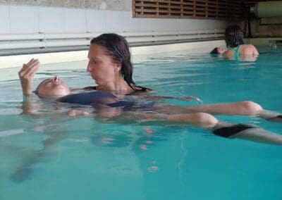 Femme en relaxation aquatique dans une piscine chauffée, bras détendus, expression sereine lors d'une séance bien-être à