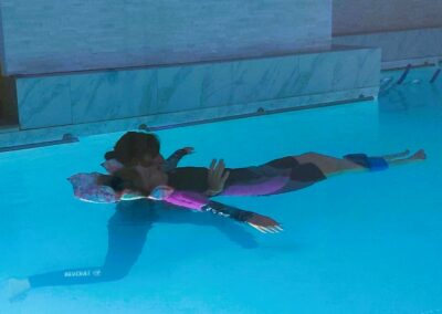Femme en posture de relaxation horizontale dans une piscine chauffée pratiquant la sophrologie aquatique pour le bien-être