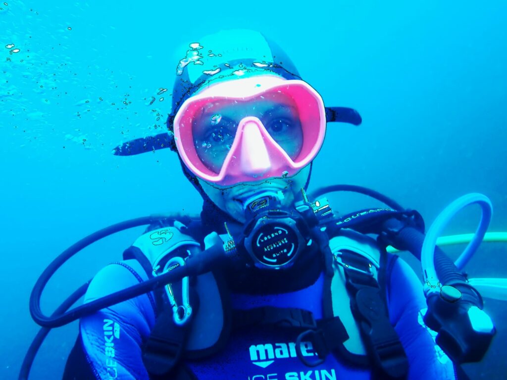 Plongeur souriant en masque rose vif explore l'océan bleu turquoise, incarnant la liberté et le bien-être aquatique en Corse