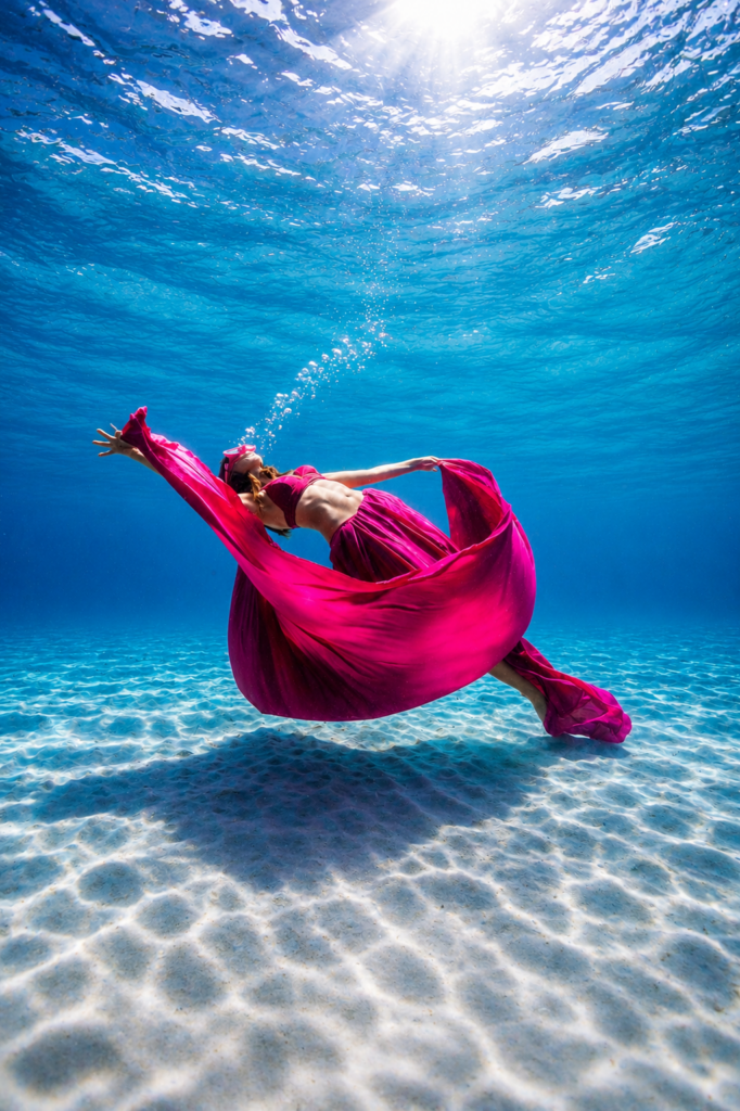 Femme en robe rose flottante pratiquant la relaxation dans l'eau turquoise, bras ouverts lors d'une séance de bien-être