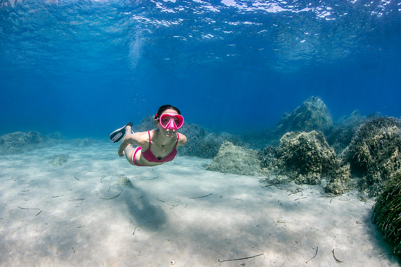 Femme en palmes et masque rose plongeant sous l'eau cristalline avec coraux à Bastia, incarnant relaxation aquatique