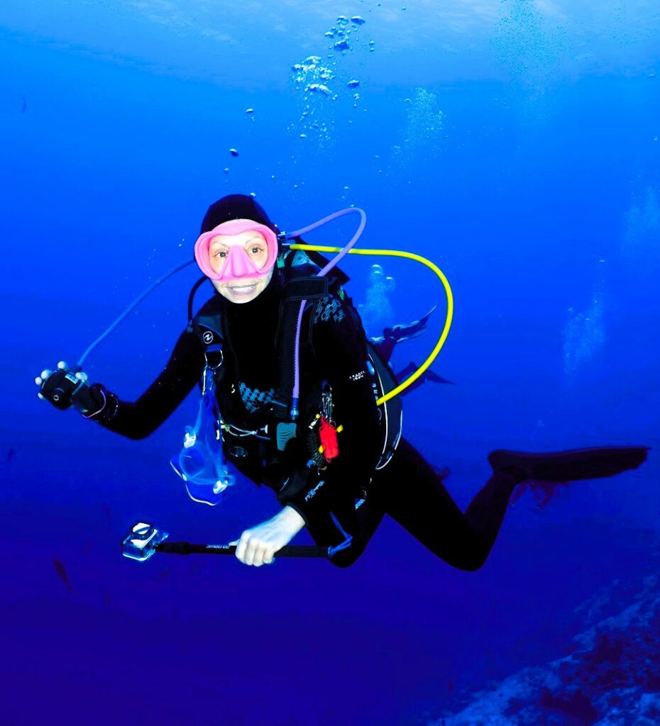 Plongeuse souriante en équipement de plongée avec masque rose dans l'eau bleue profonde illustrant la liberté aquatique